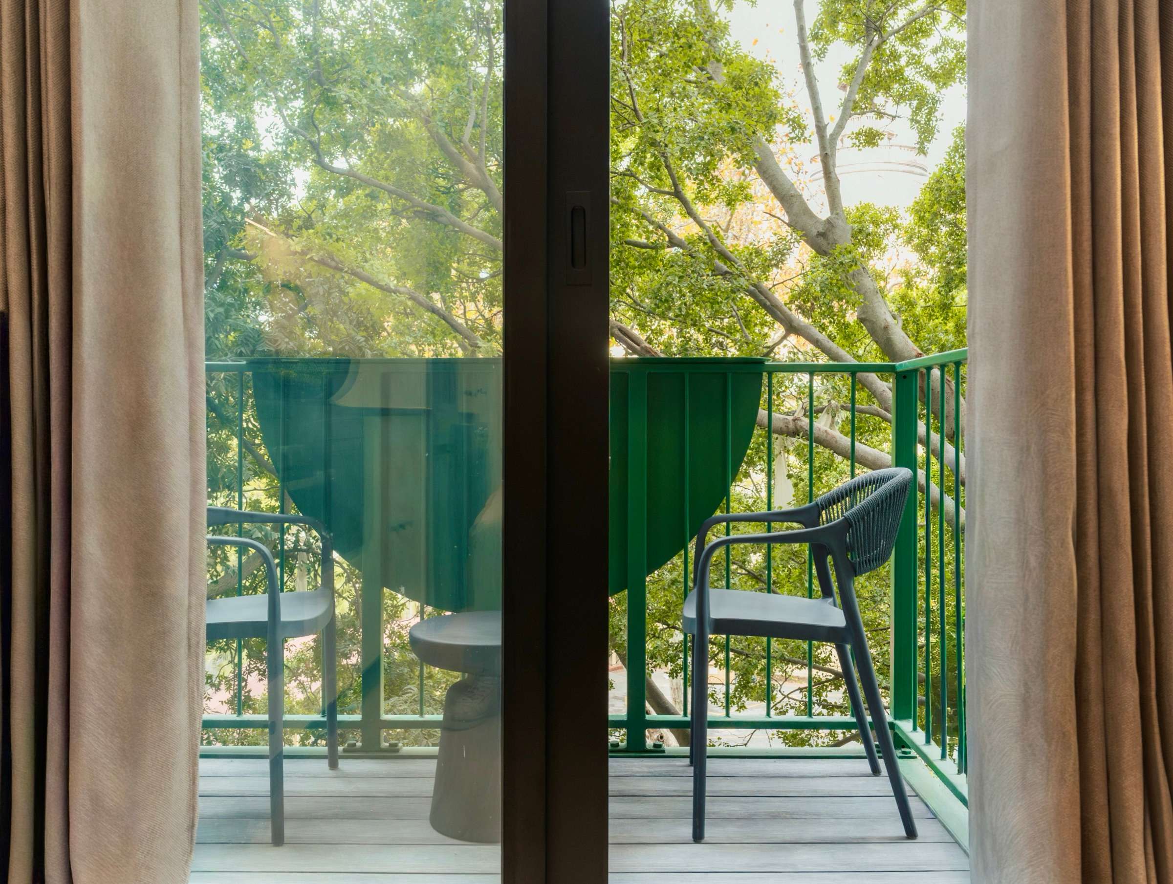Linen curtains drawn back from the balcony doors, framing a green railing and the outstretched branches of the plane tree