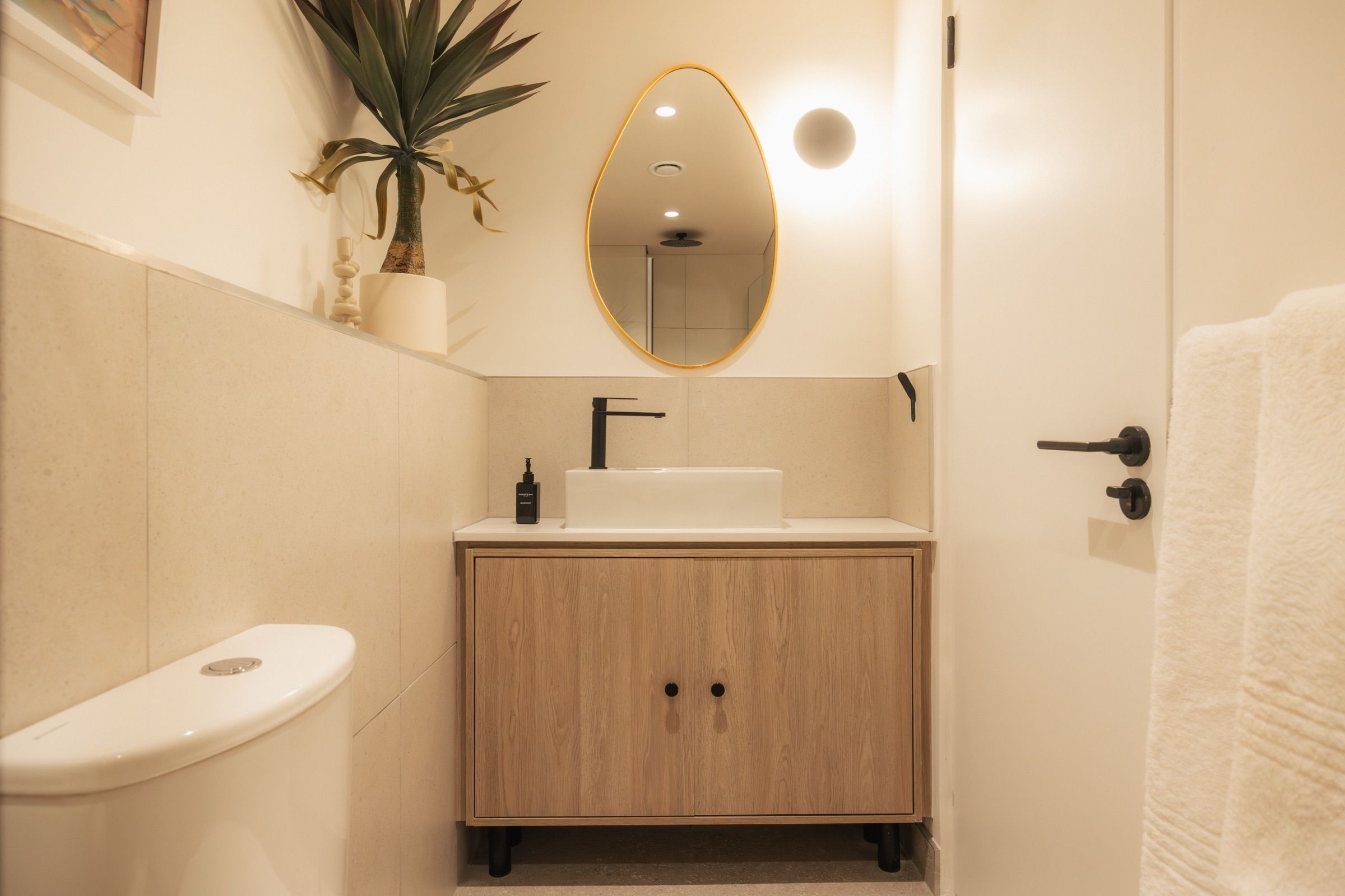 The bathroom vanity in oak with a vessel basin, a brass oval mirror and a yucca plant on the tiled ledge