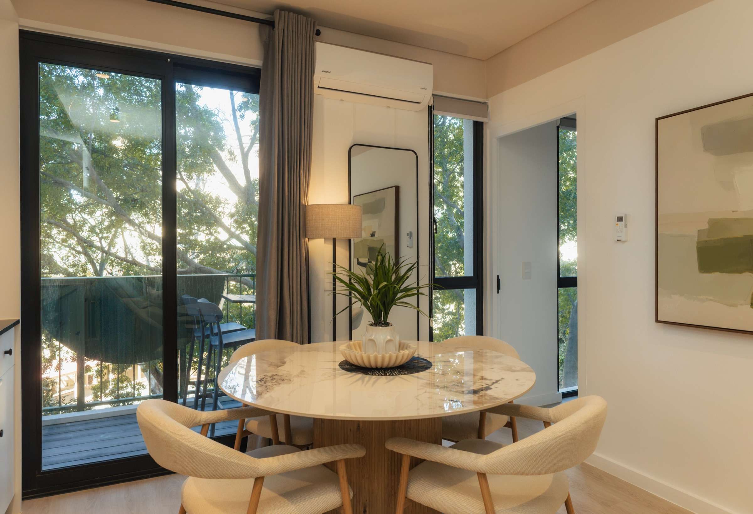 The round marble dining table and cream chairs beside floor-to-ceiling balcony doors, with the plane tree canopy filling the glass
