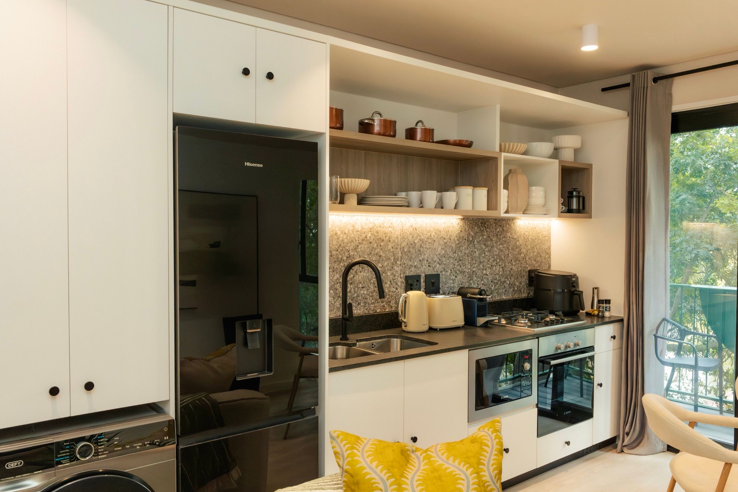 The kitchen with white cabinetry, a mosaic splashback and open oak shelves holding copper pans and stacked ceramics