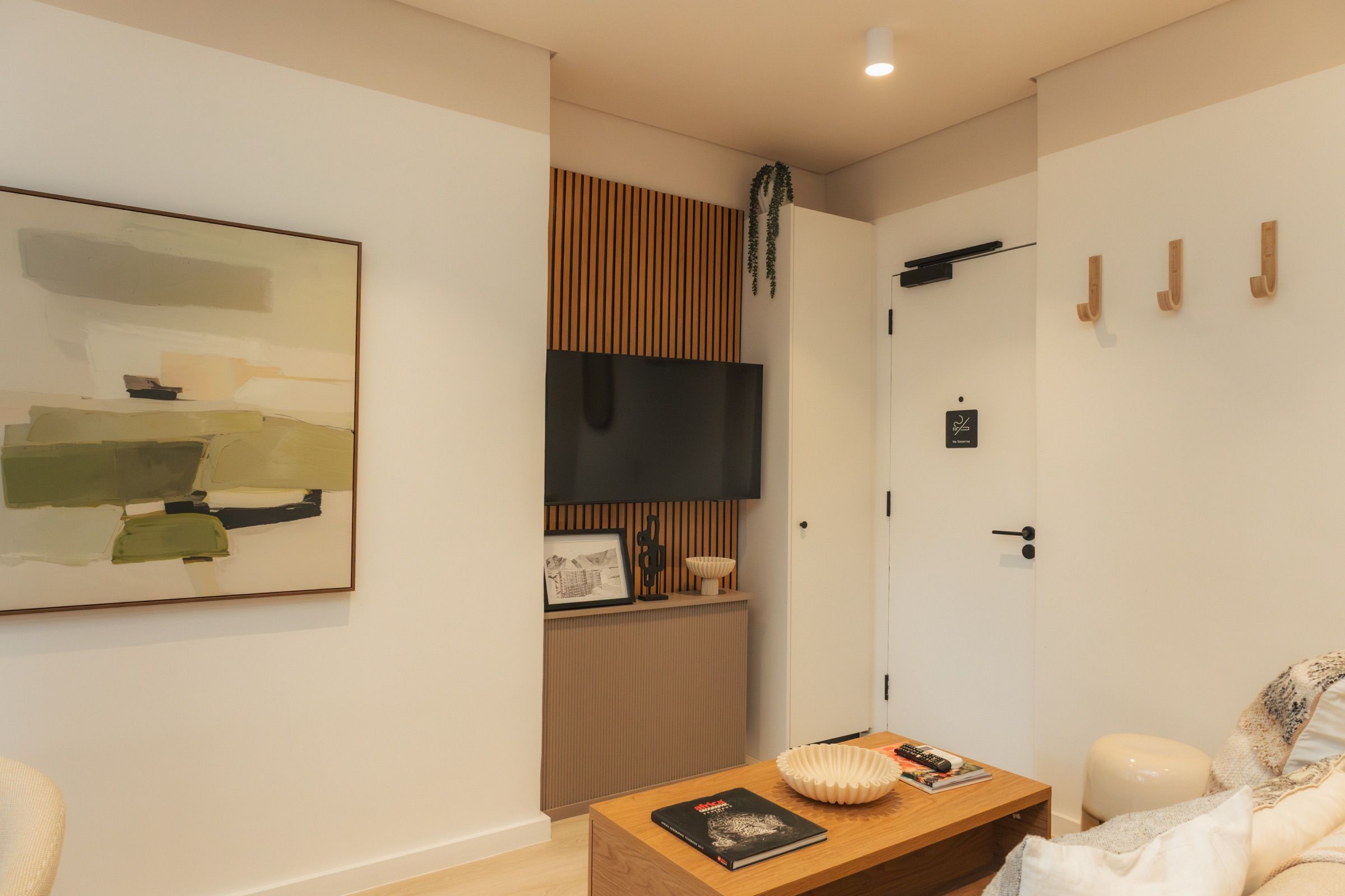 A large green and cream abstract canvas on the living room wall, beside the television mounted on its slatted oak panel